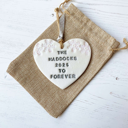Personalised first Christmas married heart ornament, pearlised white clay personalised in grey with THE HADDOCKS 2025 TO FOREVER decorated with 2 iridescent glitter snowflakes on either side of the top of the heart