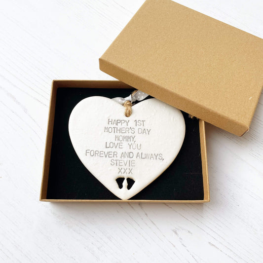 Personalised first Mother’s Day gift, pearlised white hanging clay heart with baby feet cut out at the bottom of the heart, the heart is personalised in grey with HAPPY 1ST MOTHER'S DAY MOMMY, LOVE YOU FOREVER AND ALWAYS, STEVIE XXX