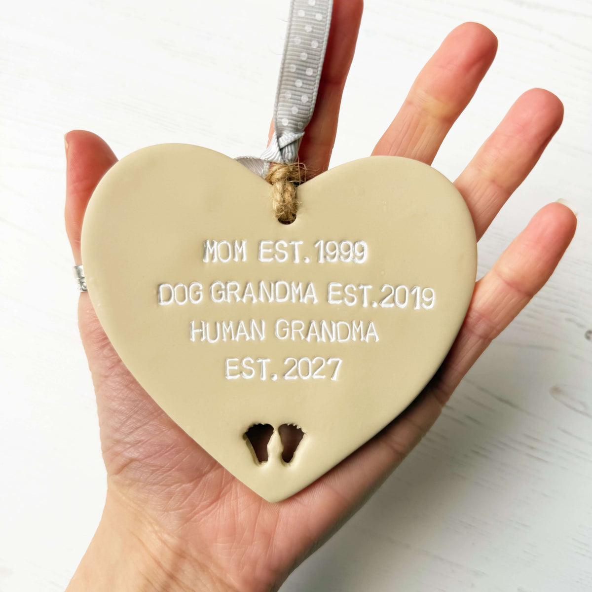 Beige clay hanging heart with baby feet cut out of the bottom and white personalisation, the heart is personalised with MOM EST. 1999 DOG  GRANDMA EST. 2019 HUMAN GRANDMA EST. 2027