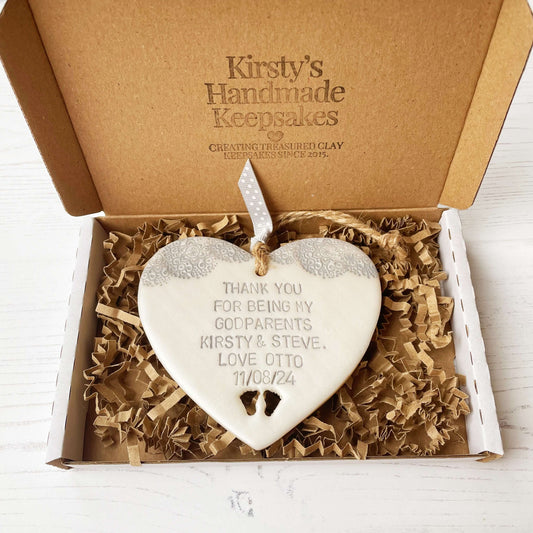 Personalised godparents gift, pearlised white clay hanging heart with baby feet cut out of the bottom and grey lace edge at the top of the heart, the heart is personalised with THANK YOU FOR BEING MY GODPARENTS KIRSTY & STEVE. LOVE OTTO 11/08/24