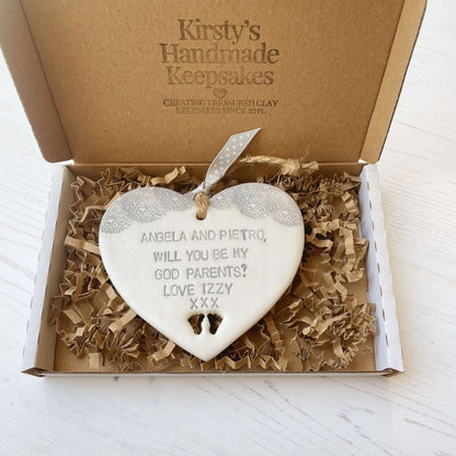 Will you be my godparents gift pearlised white clay hanging heart with baby feet cut out of the bottom grey lace edge at the top the heart is personalised with ANGELA & PIETRO, WILL YOU BE MY GODPARENTS? LOVE IZZY XXX