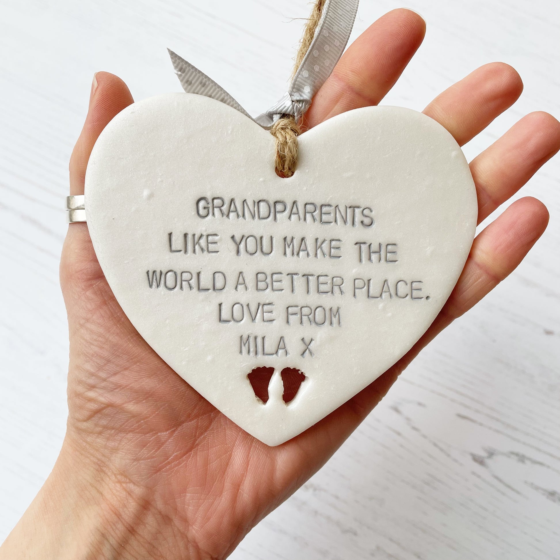 Pearlised white clay hanging heart with baby feet cut out of the bottom and grey personalisation, the heart is personalised with GRANDPARENTS LIKE YOU MAKE THE WORLD A BETTER PLACE. LOVE FROM MILA X