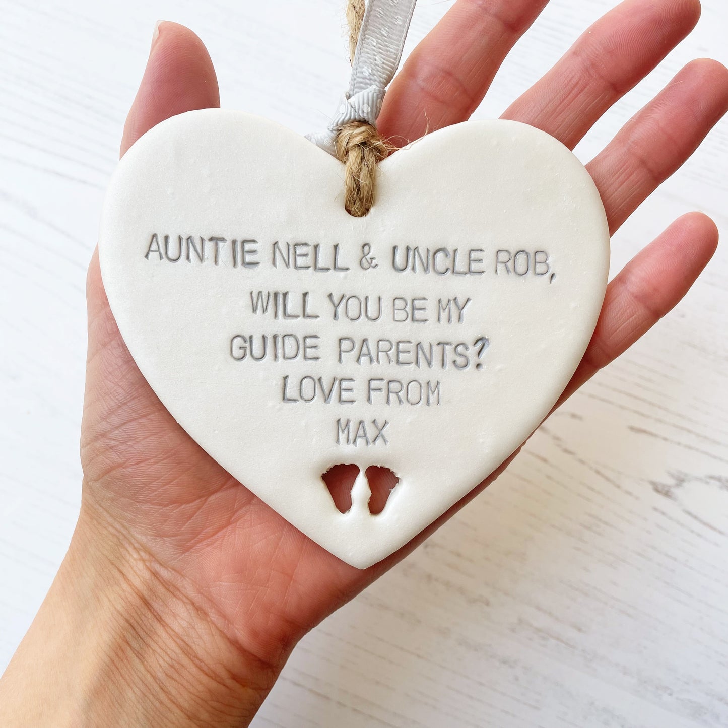 Personalised guide parent proposal gift, pearlised white clay hanging heart with baby feet cut out of the bottom, the heart is personalised with AUNTIE NELL & UNCLE ROB, WILL YOU BE MY GUIDE PARENTS? LOVE FROM MAX