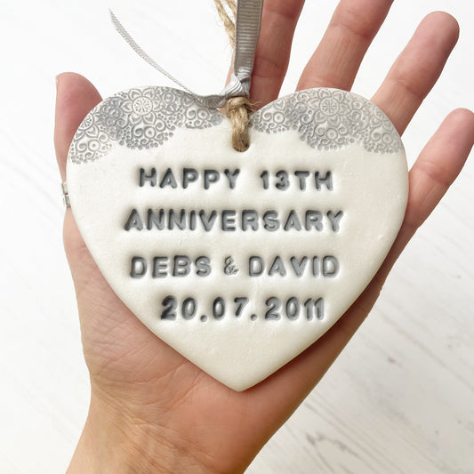 Personalised 13th anniversary gift, pearlised white clay hanging heart with a grey lace edge at the top of the heart, the heart is personalised with HAPPY 13TH ANNIVERSARY DEBS & DAVID 20.07.2011