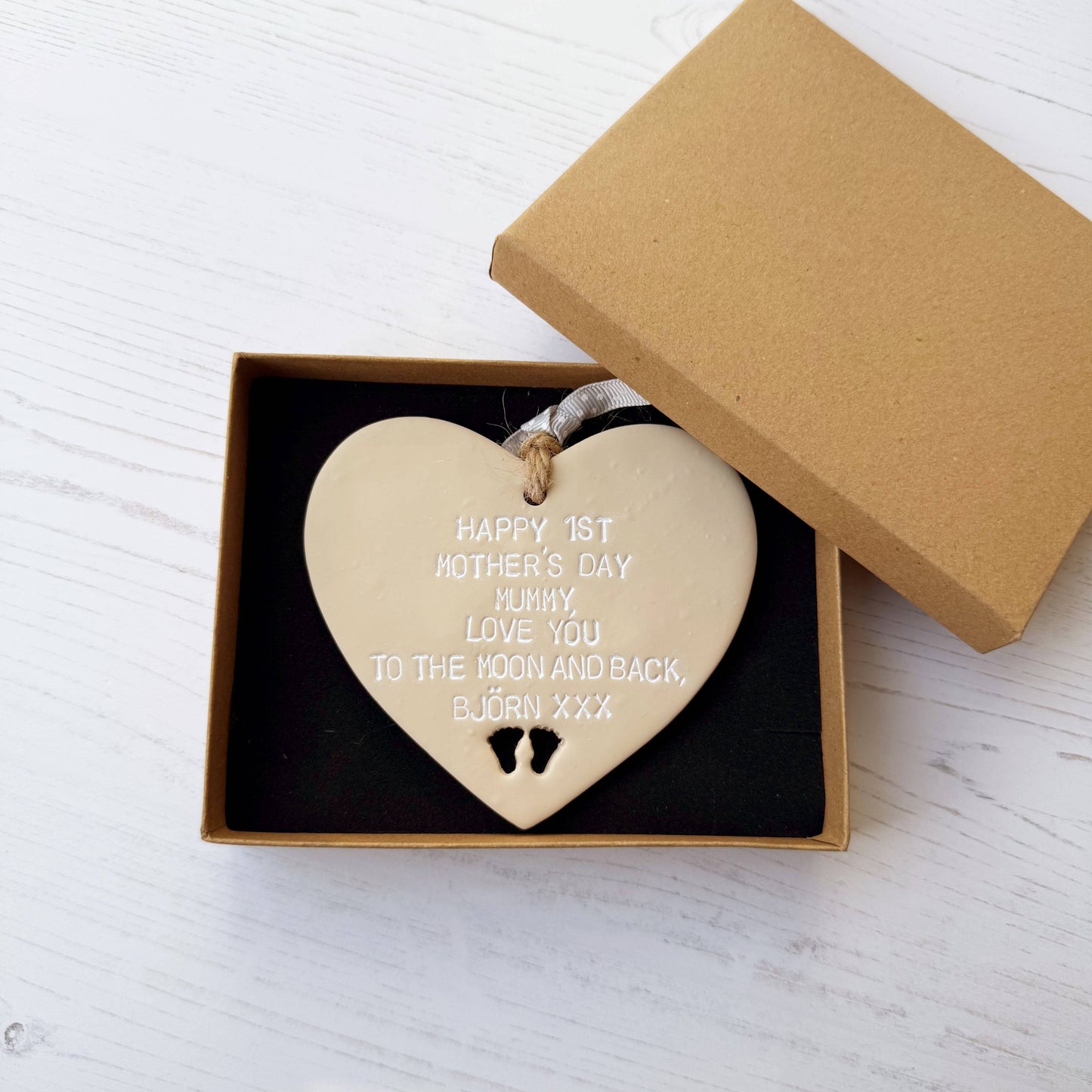 Personalised 1st Mother’s Day gift, beige clay hanging heart with baby feet cut out at the bottom of the heart, the heart is personalised with HAPPY 1ST MOTHER’S DAY MUMMY, LOVE YOU TO THE MOON AND BACK, BJÖRN XXX