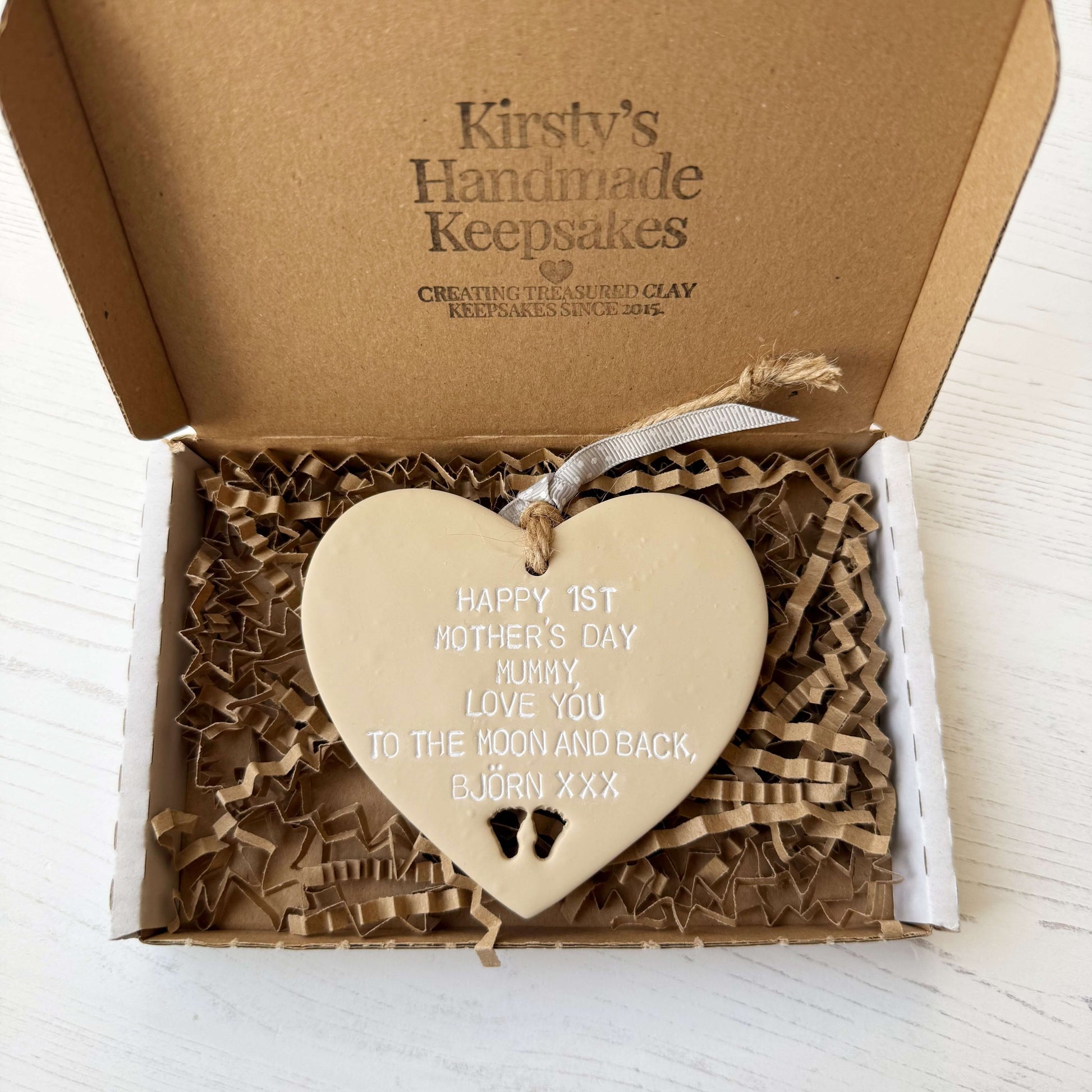 Personalised 1st Mother’s Day gift, beige clay hanging heart with baby feet cut out at the bottom of the heart, the heart is personalised with HAPPY 1ST MOTHER’S DAY MUMMY, LOVE YOU TO THE MOON AND BACK, BJÖRN XXX