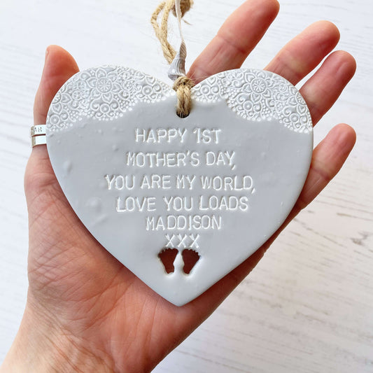 Personalised first Mother’s Day gift, grey clay hanging heart with baby feet cut out at the bottom of the heart and a white lace edge at the top of the heart, the heart is personalised with HAPPY 1ST MOTHER’S DAY, YOU ARE MY WORLD, LOVE YOU LOADS MADDISON XXX
