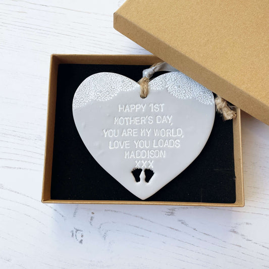 Personalised first Mother’s Day gift, grey clay hanging heart with baby feet cut out at the bottom of the heart and a white lace edge at the top of the heart, the heart is personalised with HAPPY 1ST MOTHER’S DAY, YOU ARE MY WORLD, LOVE YOU LOADS MADDISON XXX