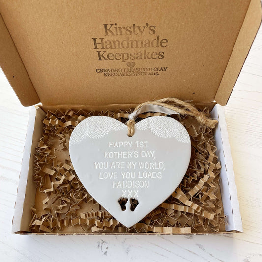Personalised first Mother’s Day gift, grey clay hanging heart with baby feet cut out at the bottom of the heart and a white lace edge at the top of the heart, the heart is personalised with HAPPY 1ST MOTHER’S DAY, YOU ARE MY WORLD, LOVE YOU LOADS MADDISON XXX