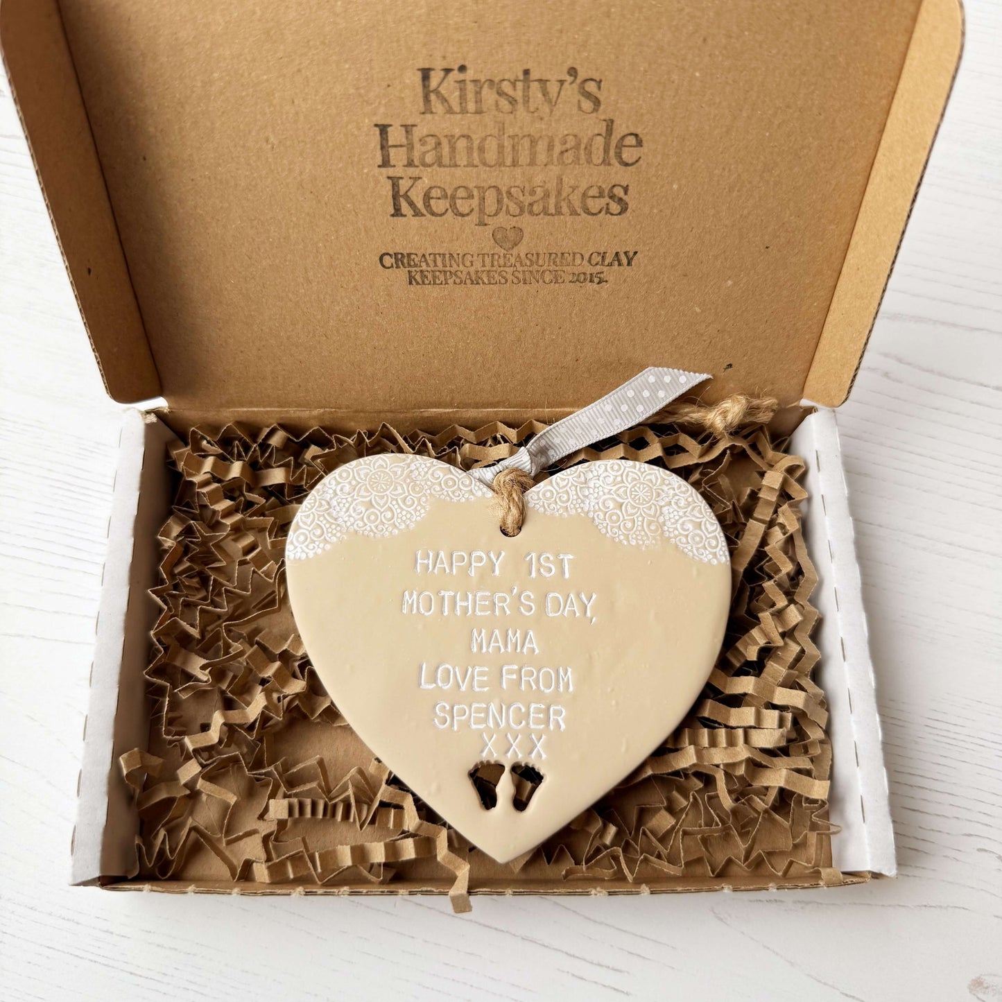 Personalised first Mother’s Day gift, beige clay hanging heart with baby feet cut out at the bottom of the heart and a white lace edge at the top of the heart, the heart is personalised with HAPPY 1ST MOTHER’S DAY MAMA, LOVE FROM SPENCER XXX