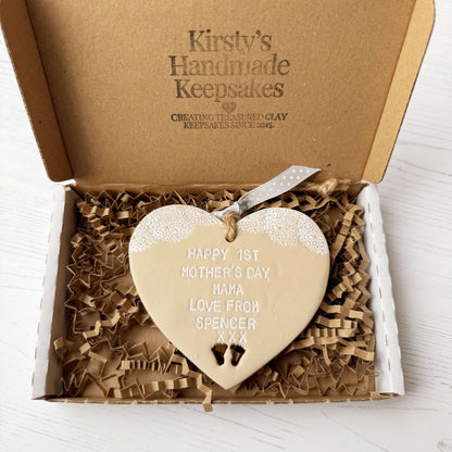 Personalised first Mother’s Day gift, beige clay hanging heart with baby feet cut out at the bottom of the heart and a white lace edge at the top of the heart, the heart is personalised with HAPPY 1ST MOTHER’S DAY MAMA, LOVE FROM SPENCER XXX
