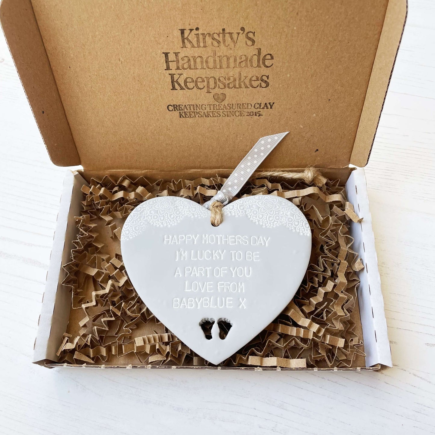 Personalised first Mother’s Day gift, grey clay hanging heart with baby feet cut out at the bottom of the heart and a white lace edge at the top of the heart, the heart is personalised with HAPPY MOTHER’S DAY I’M LUCKY TO BE A PART OF YOU LOVE FROM BABYBLUE X