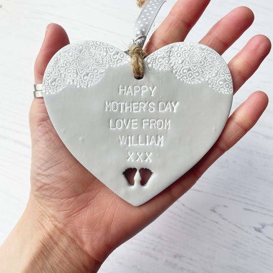 Personalised first Mother’s Day gift, grey clay hanging heart with baby feet cut out at the bottom of the heart and a white lace edge at the top of the heart, the heart is personalised with HAPPY MOTHER’S DAY LOVE FROM WILLIAM XXX
