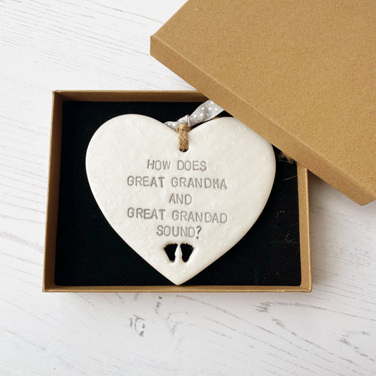 Pearlised white clay hanging heart with baby feet cut out of the bottom and grey personalisation, the heart is personalised with HOW DOES GREAT GRANDMA AND GREAT GRANDAD SOUND?