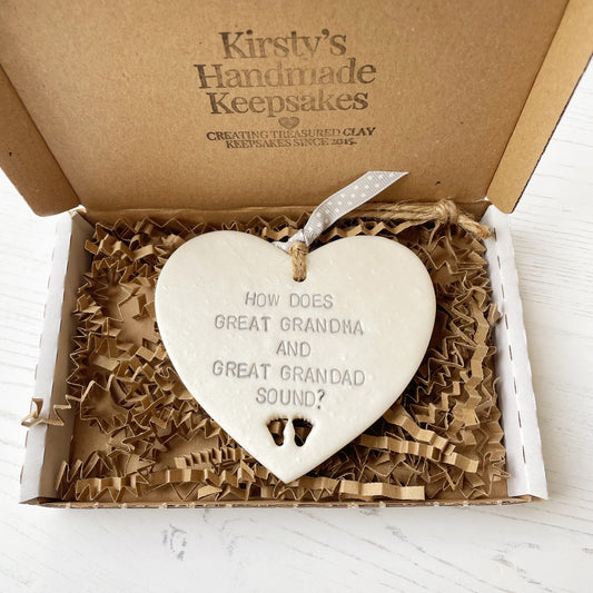 Pearlised white clay hanging heart with baby feet cut out of the bottom and grey personalisation, the heart is personalised with HOW DOES GREAT GRANDMA AND GREAT GRANDAD SOUND?