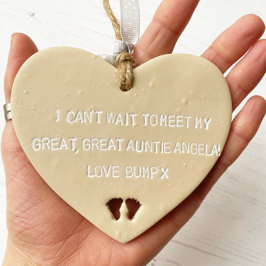 Beige clay hanging heart with baby feet cut out of the bottom and white personalisation, the heart is personalised with I CAN’T WAIT TO MEET MY GREAT GREAT AUNTIE ANGELA! LOVE BUMP X