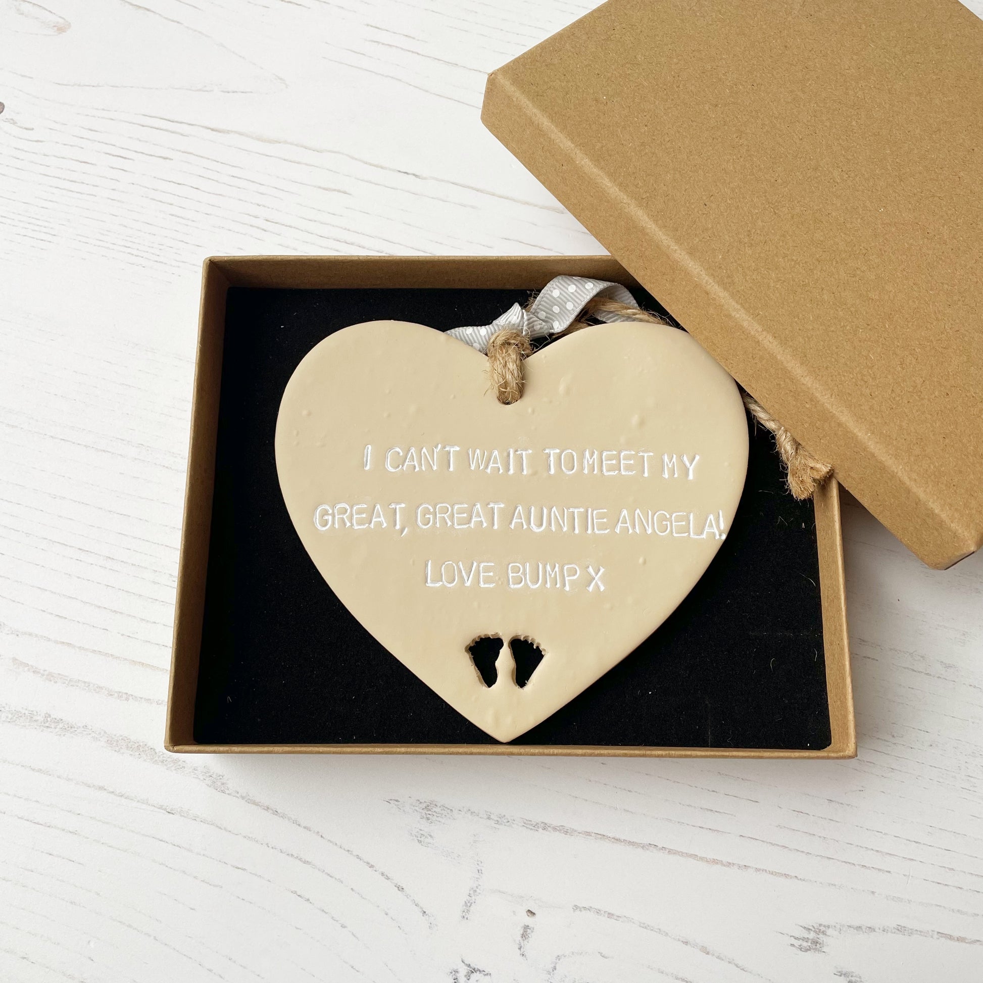 Beige clay hanging heart with baby feet cut out of the bottom and white personalisation, the heart is personalised with I CAN’T WAIT TO MEET MY GREAT GREAT AUNTIE ANGELA! LOVE BUMP X