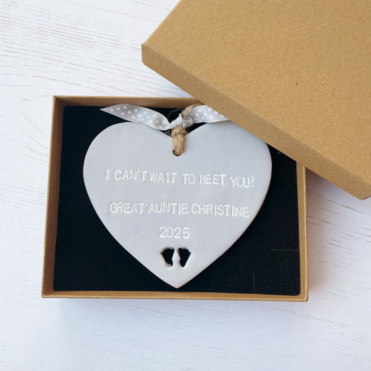 Grey clay hanging heart with baby feet cut out of the bottom and white personalisation, the heart is personalised with I CAN’T WAIT TO MEET YOU! GREAT AUNTIE CHRISTINE 2025