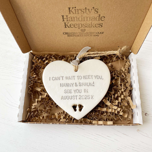 Pearlised white clay hanging heart with baby feet cut out of the bottom and grey personalisation, the heart is personalised with I CAN’T WAIT TO SEE YOU AND BY LOVED BY YOU. I LOVE YOU BABY BUD X