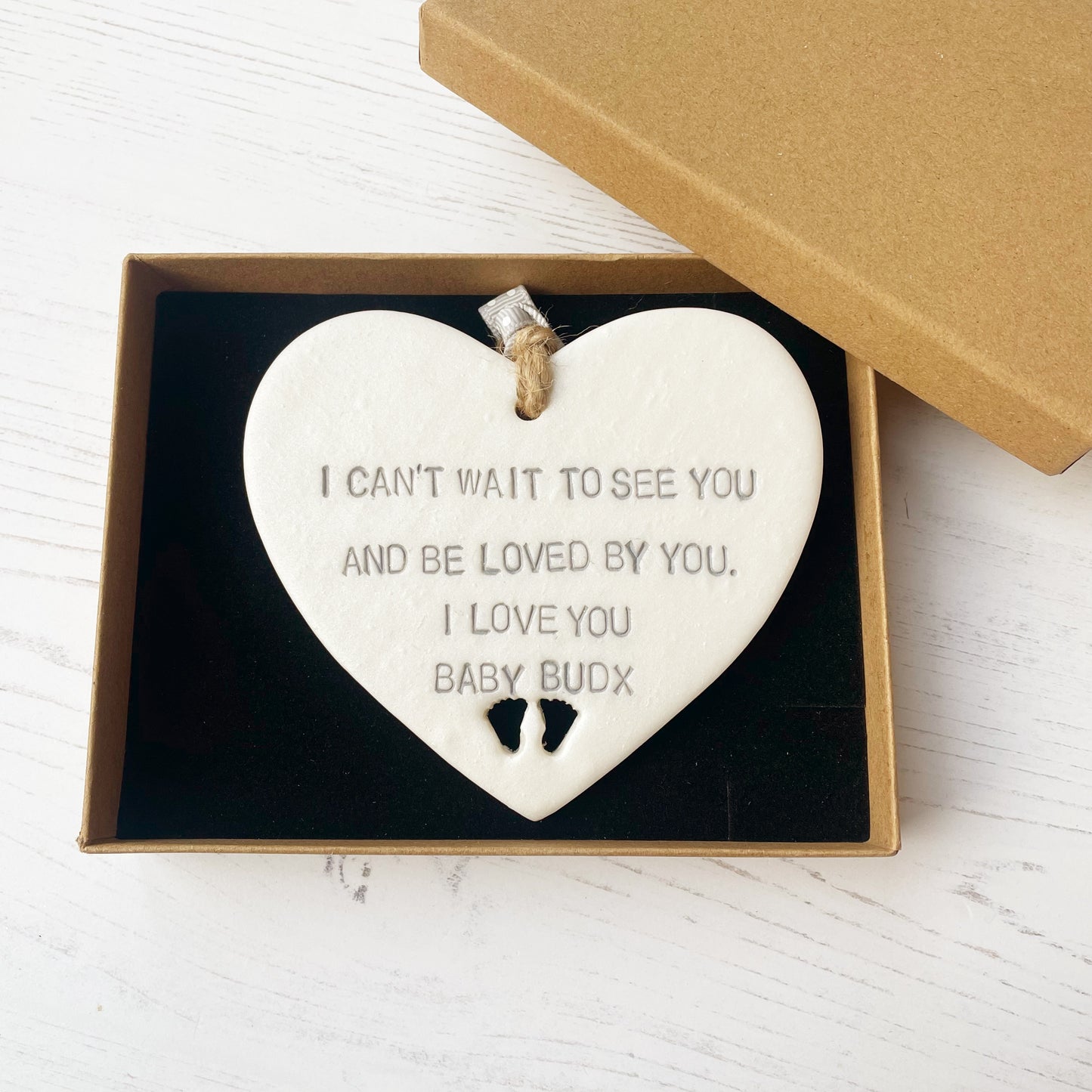 Pearlised white clay hanging heart with baby feet cut out of the bottom and grey personalisation, the heart is personalised with I CAN’T WAIT TO SEE YOU AND BY LOVED BY YOU. I LOVE YOU BABY BUD X