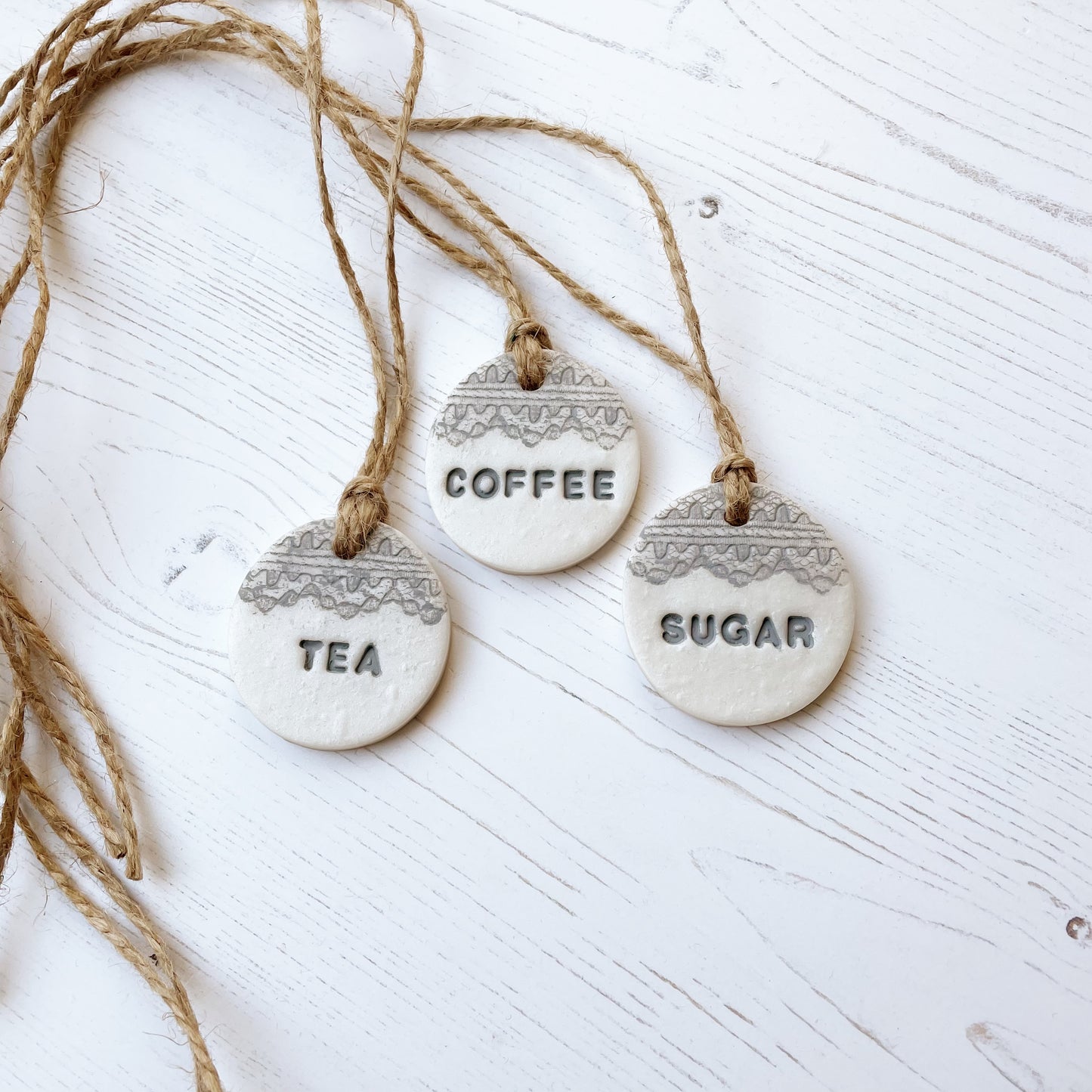 3 round pearlised white clay kitchen canister labels with coffee, tea  and sugar stamped on each label in grey with a lace edge top