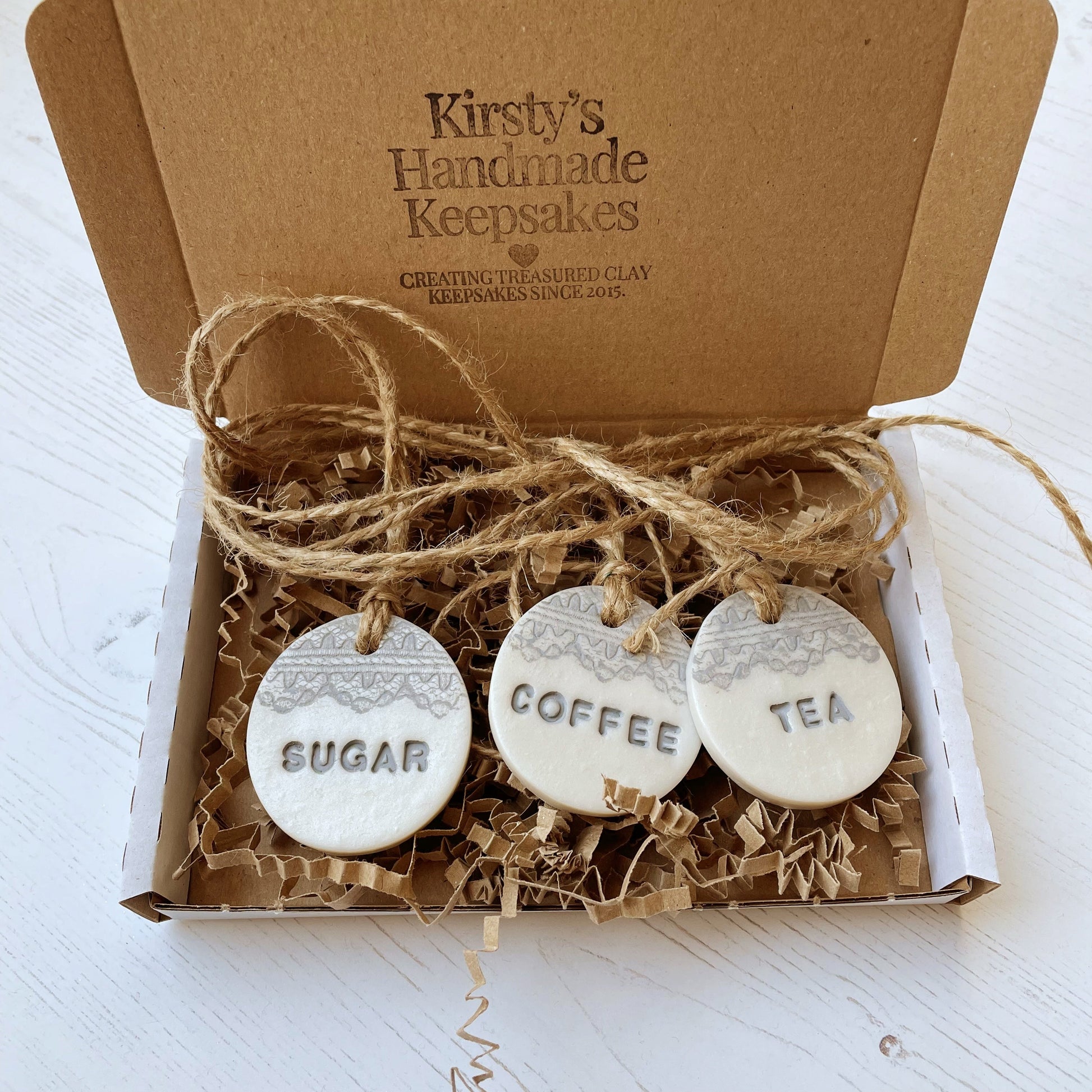 3 round pearlised white clay kitchen canister labels with coffee, tea  and sugar stamped on each label in grey with a lace edge top. In a postal box with Kraft Zigzag paper