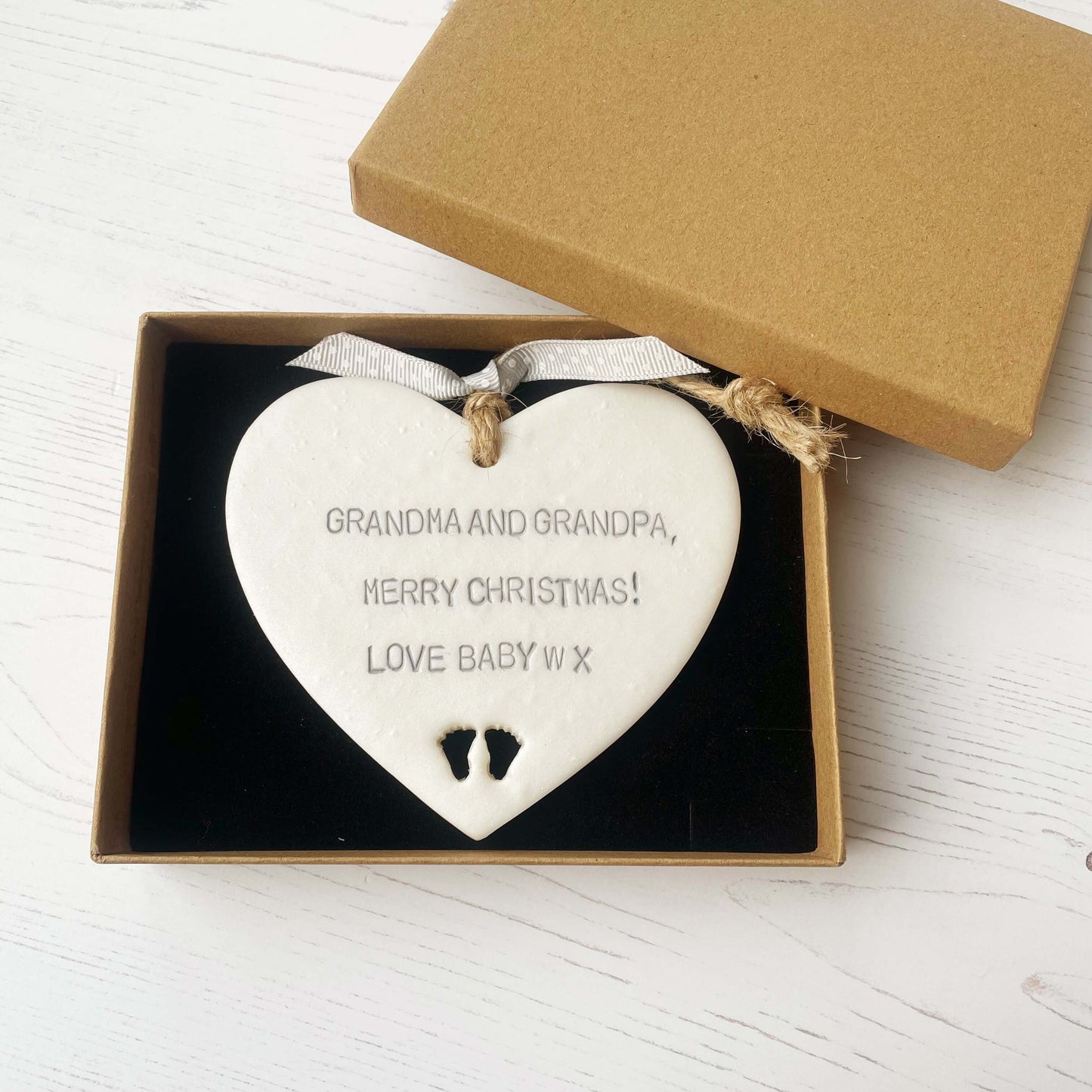 Pearlised white clay hanging heart with baby feet cut out of the bottom and grey personalisation, the heart is personalised with GRANDMA & GRANDPA, MERRY CHRISTMAS! LOVE BABY W X