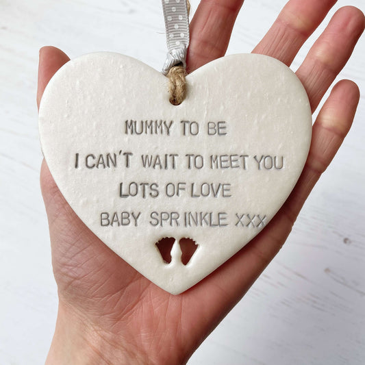 Personalised Mother’s Day gift, pearlised white clay hanging heart with baby feet cut out at the bottom of the heart, the heart is personalised with MUMMY TO BE I CAN’T WAIT TO MEET YOU LOTS OF LOVE BABY SPRINKLE XXX