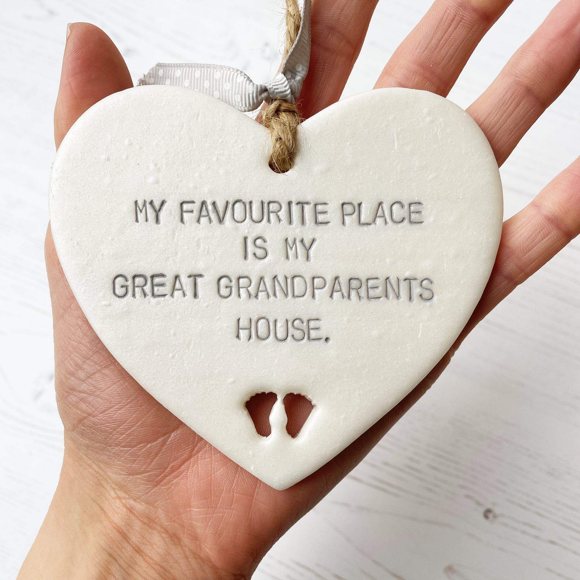 Pearlised white clay hanging heart with baby feet cut out of the bottom and grey personalisation, the heart is personalised with MY FAVOURITE PLACE IS MY GREAT GRANDPARENTS HOUSE.