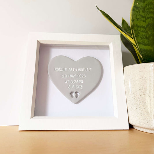 Personalised baby keepsake gift, grey clay heart with baby feet cut out at the bottom of the heart in a white box frame, the heart is personalised with the baby’s name, date of birth, weight and time
