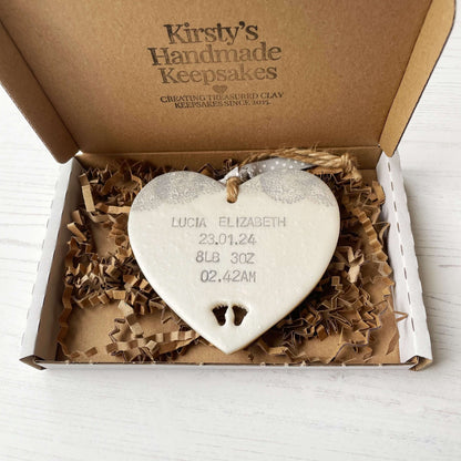 Personalised baby keepsake gift, pearlised white clay hanging heart with baby feet cut out at the bottom of the heart and a grey lace edge at the top of the heart, the heart is personalised with the baby’s name, date of birth, weight and time