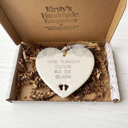 Personalised baby keepsake gift, pearlised white clay hanging heart with baby feet cut out at the bottom of the heart and a grey lace edge at the top of the heart, the heart is personalised with the baby’s name, date of birth, weight and time