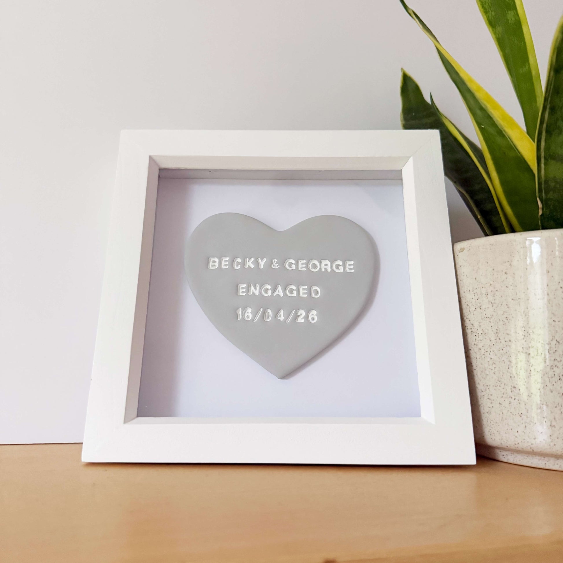 Personalised framed engagement gift, grey clay heart in a white box frame, the heart is personalised in white with BECKY & GEORGE ENGAGED 16/04/26