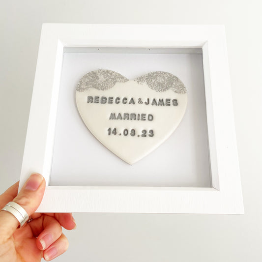 Personalised framed wedding gift, pearlised white clay heart with a grey lace edge at the top of the heart in a white box frame, the heart is personalised with REBECCA & JAMES MARRIED 14.08.23