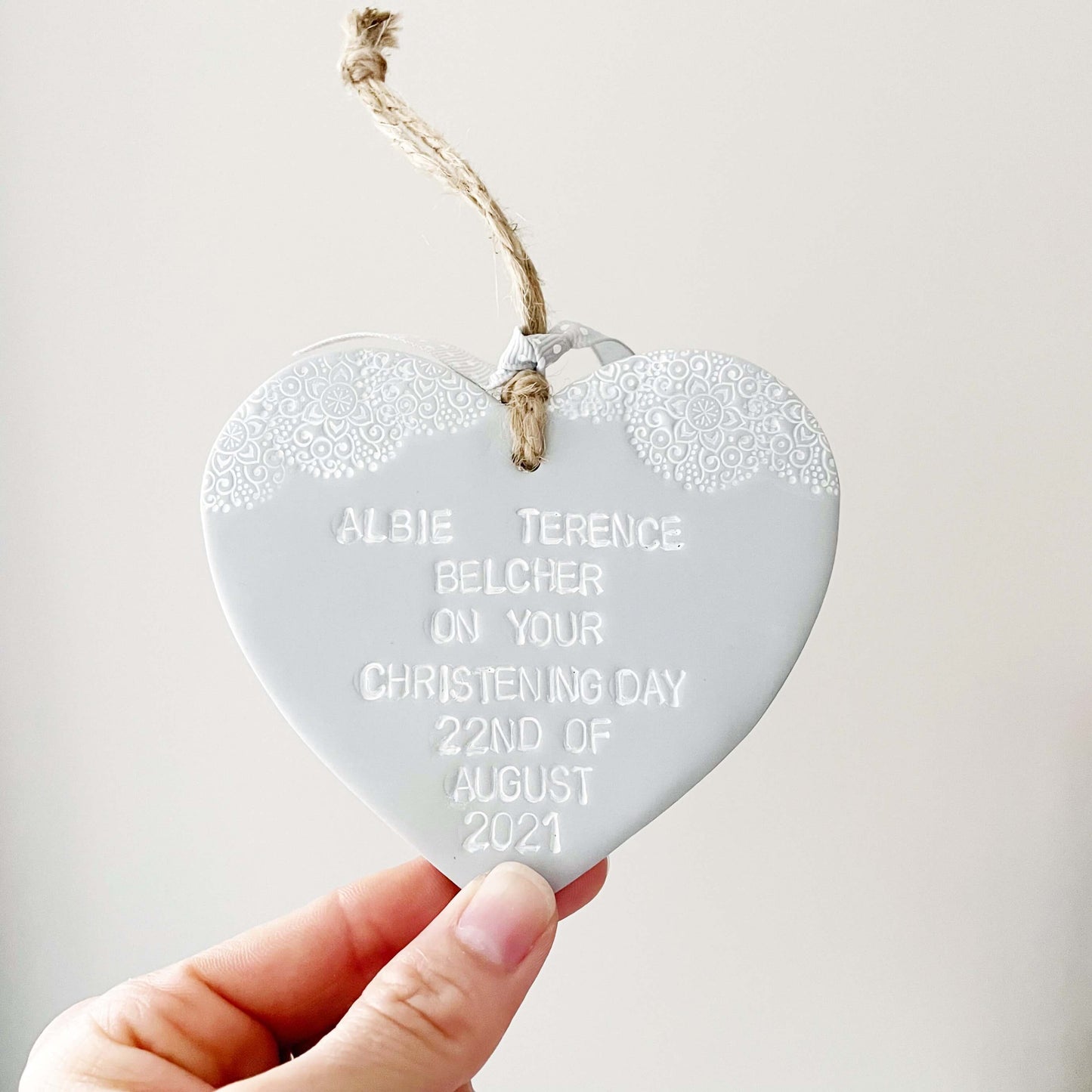 Personalised Christening baptism gift, grey clay hanging heart with a white lace edge at the top of the heart, the heart is personalised with ALBIE TERENCE BELCHER ON YOUR CHRISTENING DAY 22ND OF AUGUST 2021