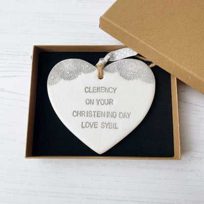 Personalised Christening baptism gift, Pearlised white clay hanging heart with a grey lace edge at the top of the heart, the heart is personalised with CLEMENCY ON YOUR CHRISTENING DAY LOVE SYBIL
