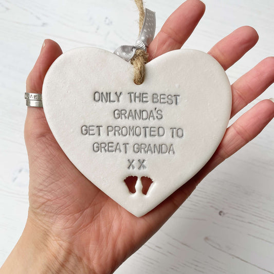 Pearlised white clay hanging heart pregnancy reveal with baby feet cut out of the bottom and grey personalisation, the heart is personalised with ONLY THE BEST GRANDA’S GET PROMOTED TO GREAT GRANDA XX