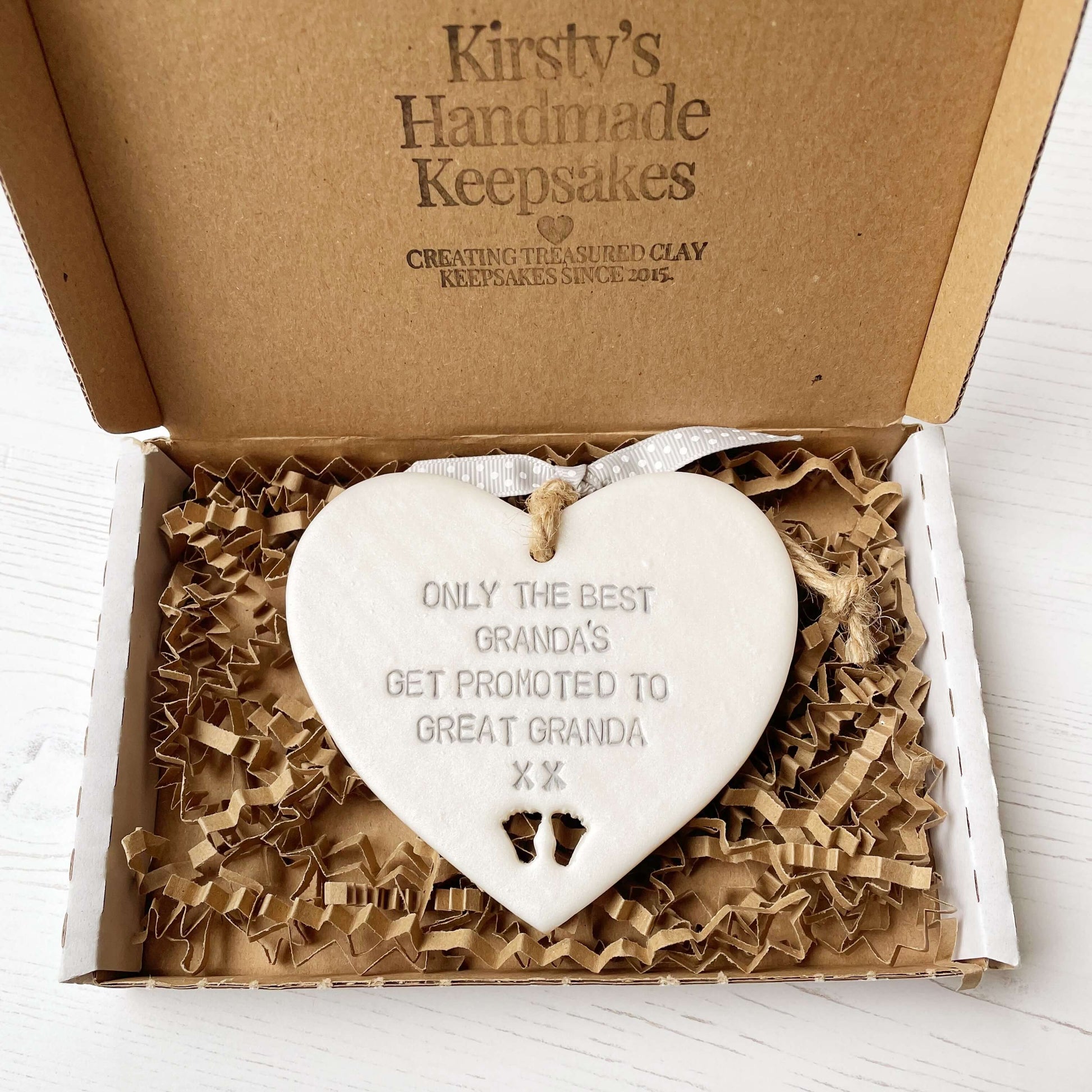 Pearlised white clay hanging heart pregnancy reveal with baby feet cut out of the bottom and grey personalisation, the heart is personalised with ONLY THE BEST GRANDA’S GET PROMOTED TO GREAT GRANDA XX