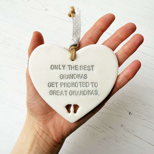 Pearlised white clay hanging heart with baby feet cut out of the bottom and grey personalisation, the heart is personalised with ONLY THE BEST GRANDMAS GET PROMOTED TO GREAT GRANDMAS
