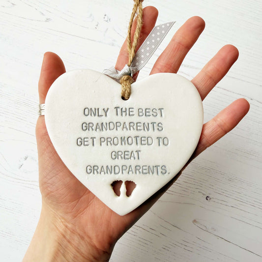 Pearlised white clay hanging heart with baby feet cut out of the bottom and grey personalisation, the heart is personalised with ONLY THE BEST GRANDPARENTS GET PROMOTED TO GREAT GRANDPARENTS