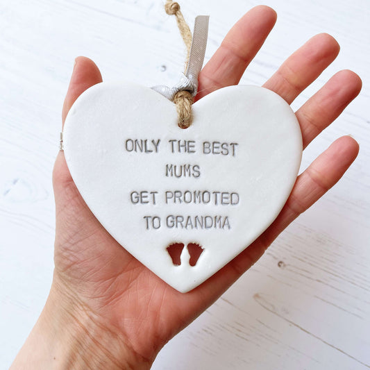 Pearlised white clay hanging heart with baby feet cut out of the bottom and grey personalisation, the heart is personalised with ONLY THE BEST MUMS GET PROMOTED TO GRANDMA
