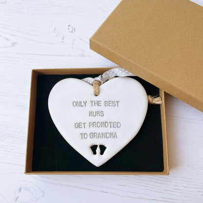 Pearlised white clay hanging heart with baby feet cut out of the bottom and grey personalisation, the heart is personalised with ONLY THE BEST MUMS GET PROMOTED TO GRANDMA