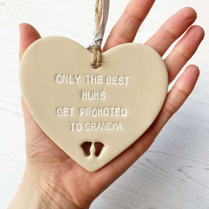 Beige clay hanging heart with baby feet cut out of the bottom and white personalisation, the heart is personalised with ONLY THE BEST MUMS GET PROMOTED TO GRANDMA