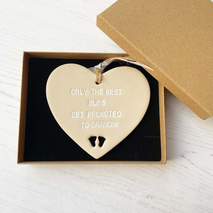 Beige clay hanging heart with baby feet cut out of the bottom and white personalisation, the heart is personalised with ONLY THE BEST MUMS GET PROMOTED TO GRANDMA
