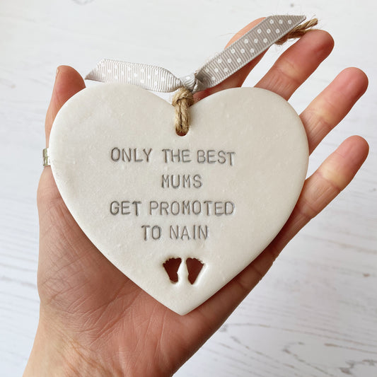 Pearlised white clay hanging heart with baby feet cut out of the bottom and grey personalisation, the heart is personalised with ONLY THE BEST MUMS GET PROMOTED TO NAIN