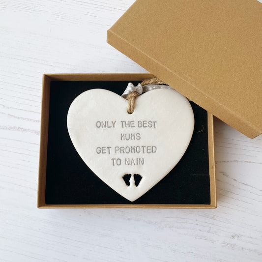 Pearlised white clay hanging heart with baby feet cut out of the bottom and grey personalisation, the heart is personalised with ONLY THE BEST MUMS GET PROMOTED TO NAIN