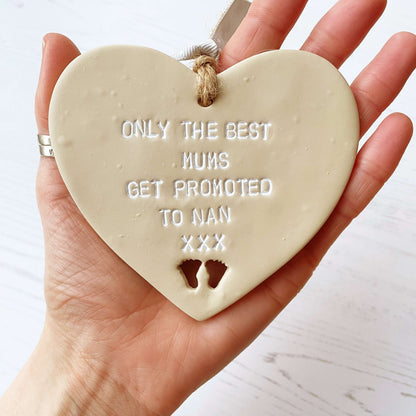 Beige clay hanging heart with baby feet cut out of the bottom and white personalisation, the heart is personalised with ONLY THE BEST MUMS GET PROMOTED TO NAN XXX