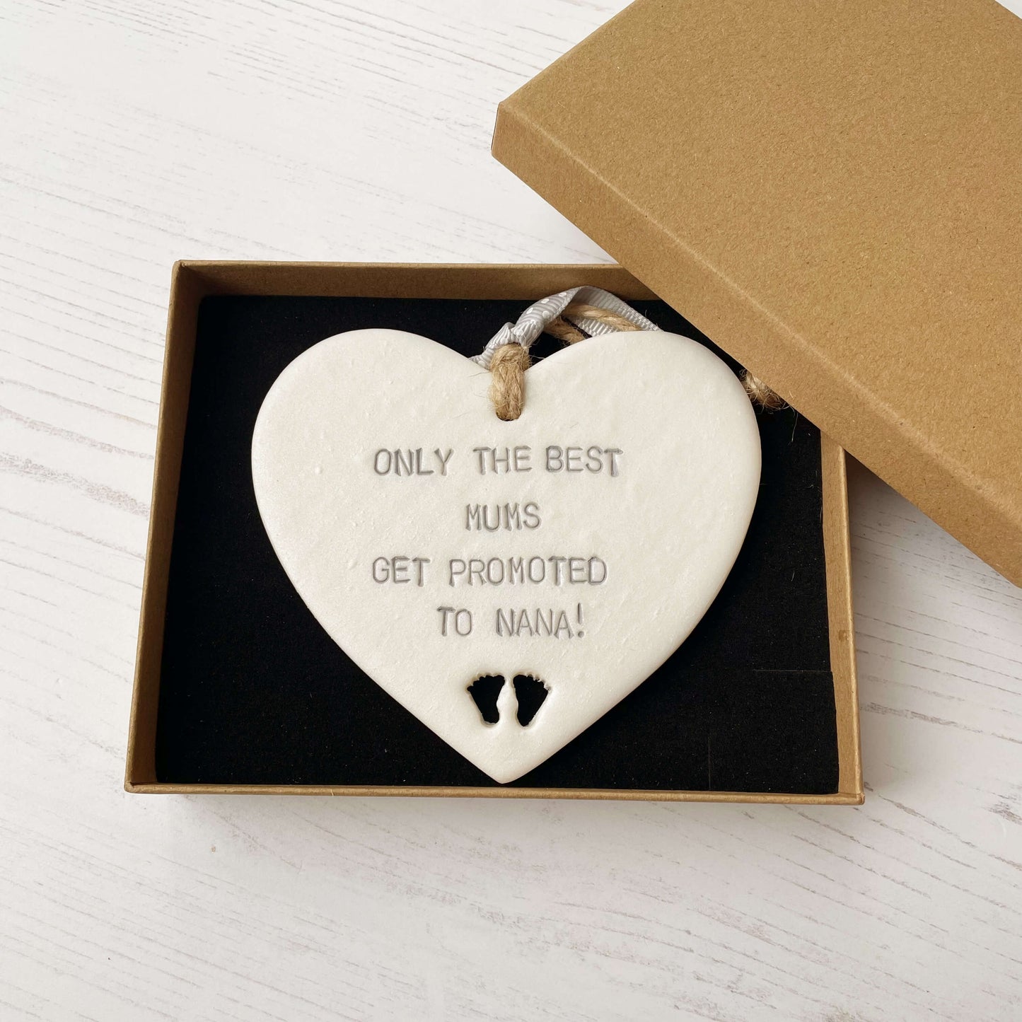 Pearlised white clay hanging heart with baby feet cut out of the bottom and grey personalisation, the heart is personalised with ONLY THE BEST MUMS GET PROMOTED TO NANA!