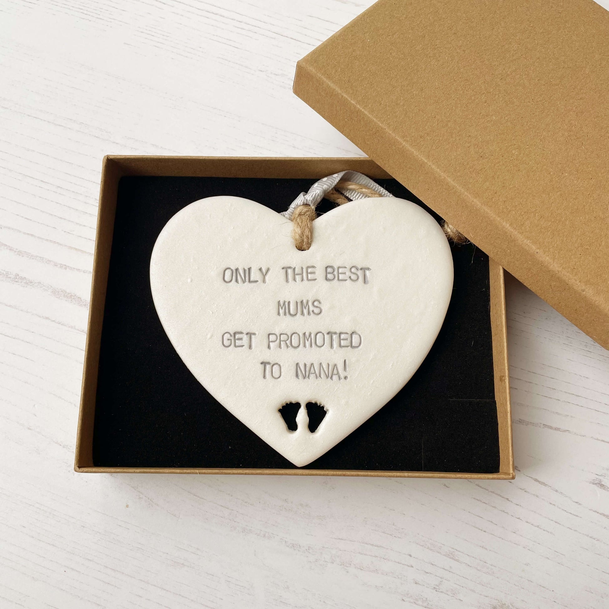 Pearlised white clay hanging heart with baby feet cut out of the bottom and grey personalisation, the heart is personalised with ONLY THE BEST MUMS GET PROMOTED TO NANA!