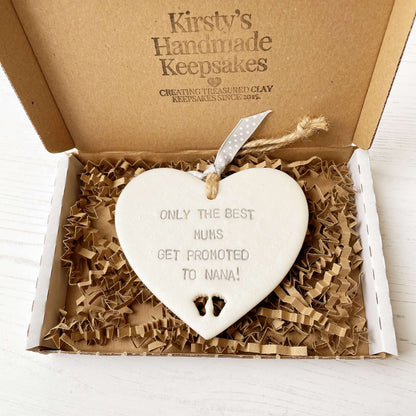 Pearlised white clay hanging heart with baby feet cut out of the bottom and grey personalisation, the heart is personalised with ONLY THE BEST MUMS GET PROMOTED TO NANA!